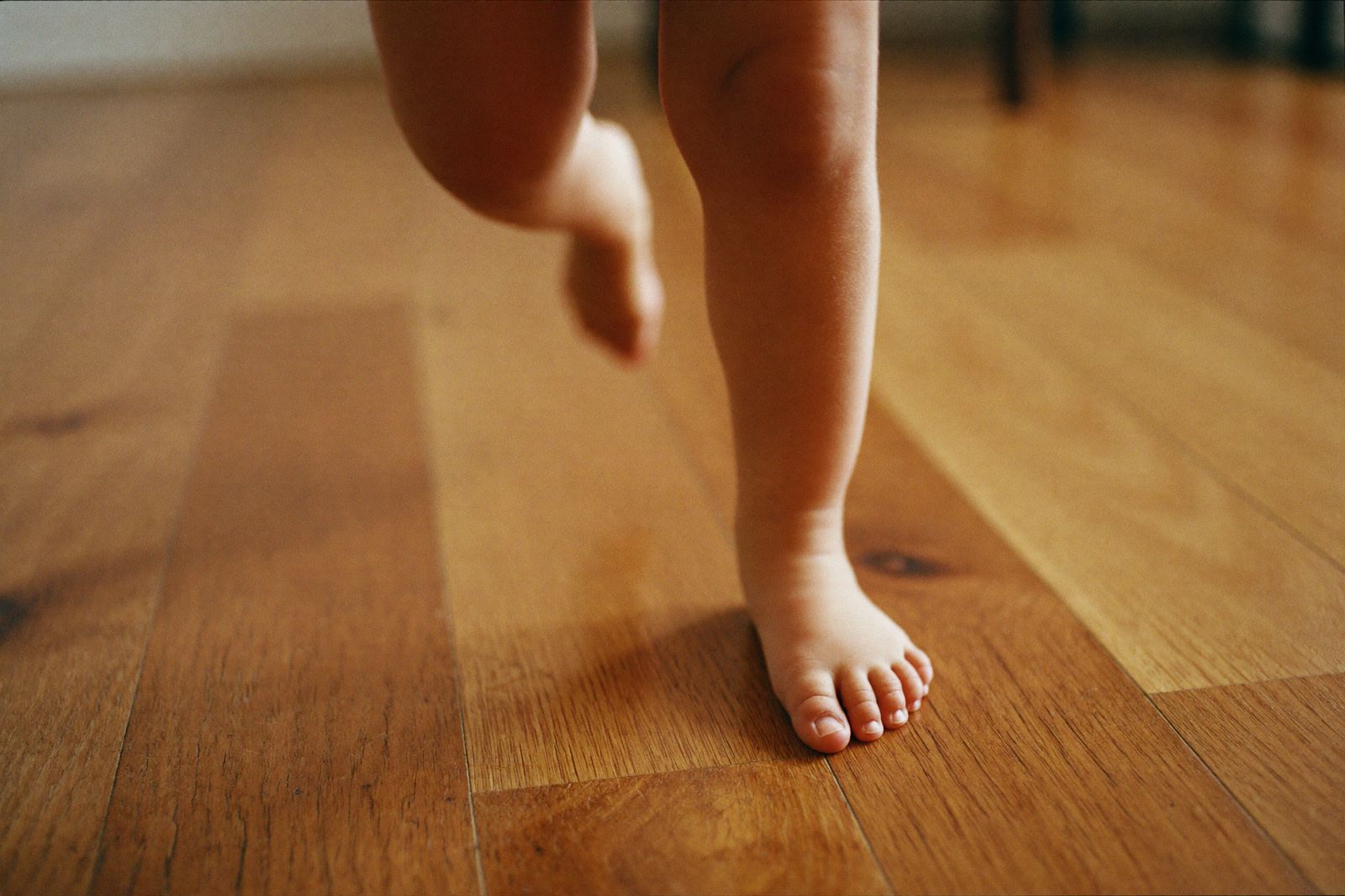 A toddler's bare feet running across a warm wooden floor