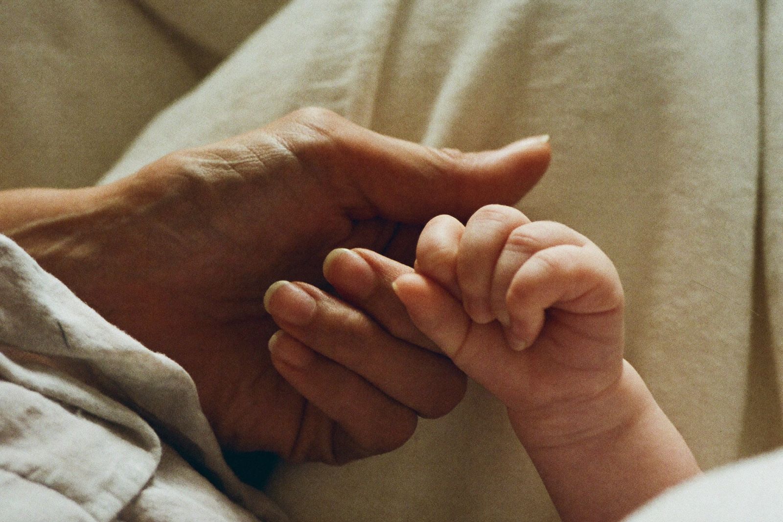A grandparent's hand gently holding a newborn's tiny hand